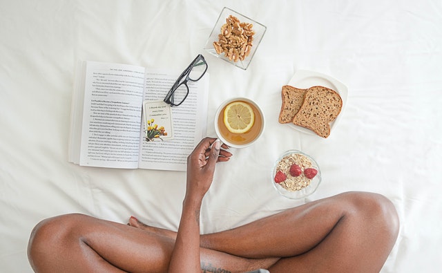 Person holding white ceramic mug with lemon near book and 1065588
