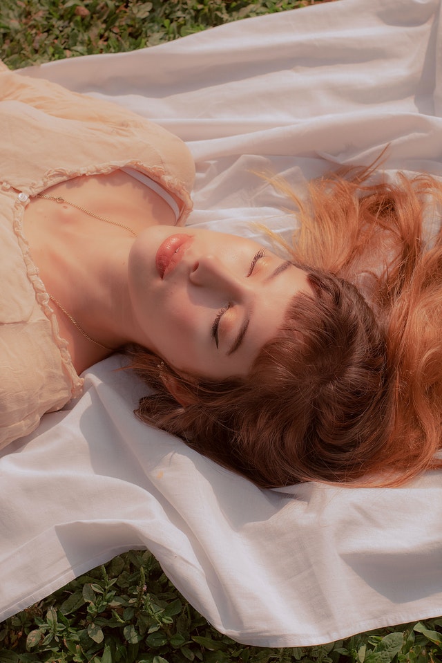 Woman with eyes closed lying on white textile 3960803