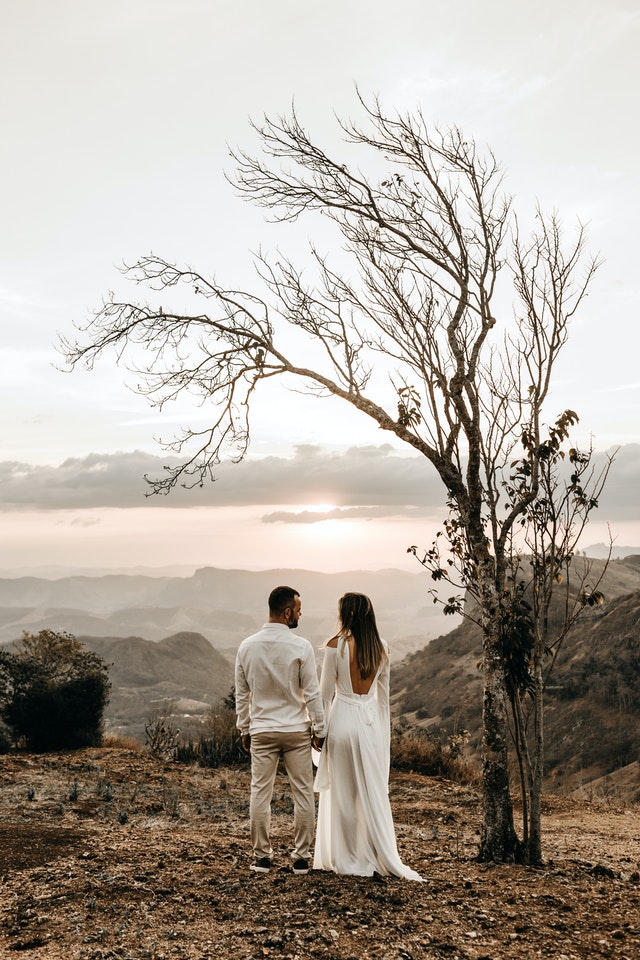 A couple in white dress standing in view of the mountain 2917382