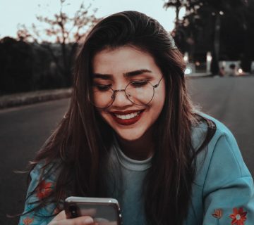 Photo of woman smiling while looking at smartphone 2465327 360x320