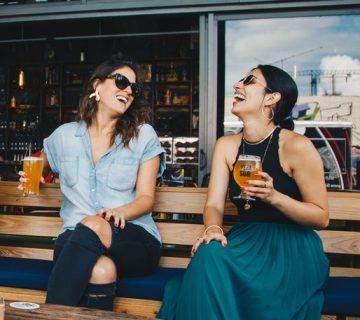 Two smiling women sitting on wooden bench 1267696 360x320